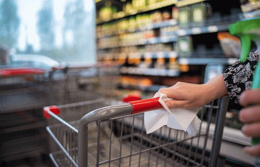 Woman wiping down grocery cart in supermarket