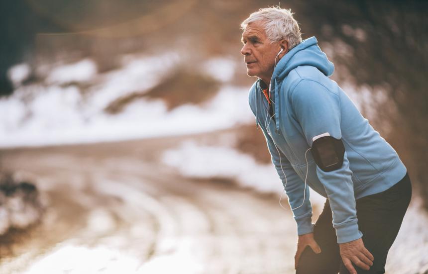 older man listening to music taking a break from running during the winter