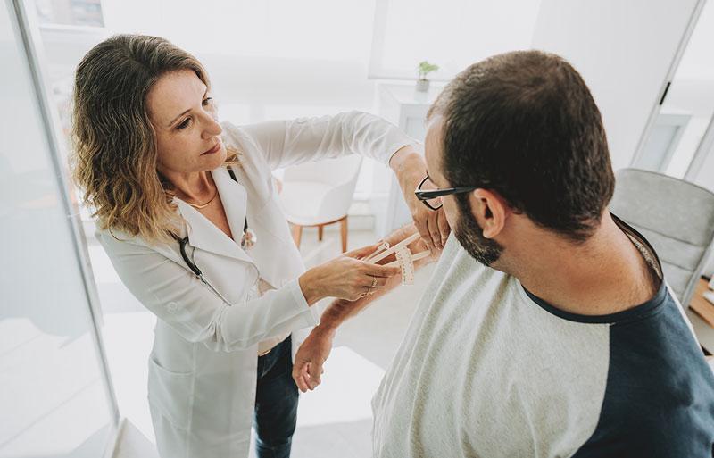 Female physician measuring body fat of male patient with skinfold calipers