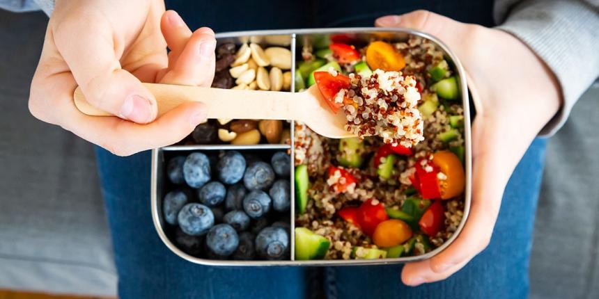 Person using spoon to lift fruit, nuts, vegetables and grains from a food tray