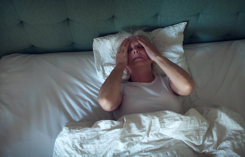 older woman laying in bed gripping sides of head